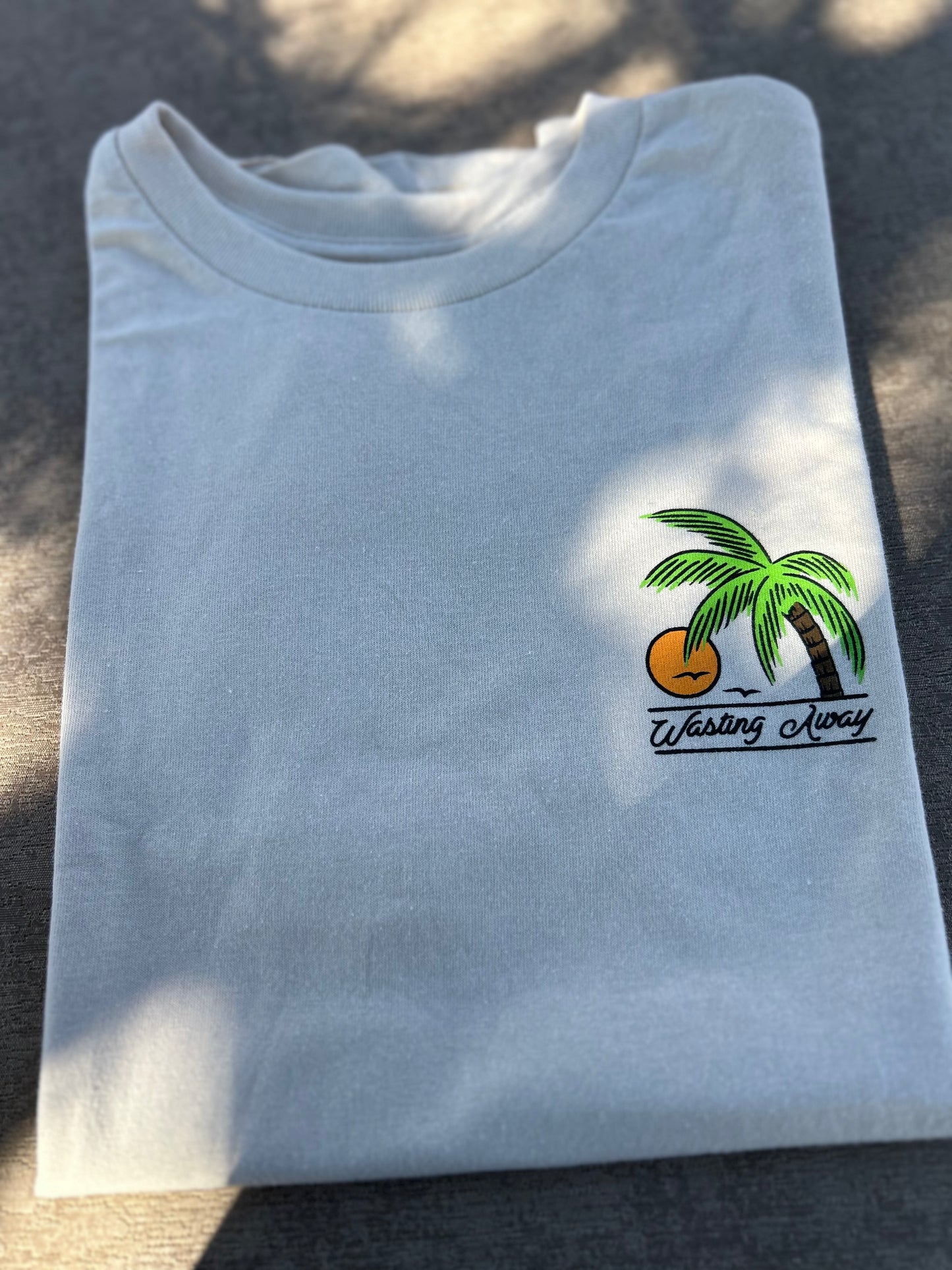 Folded cream colored t-shirt with a palm tree and sun design on a dark surface
