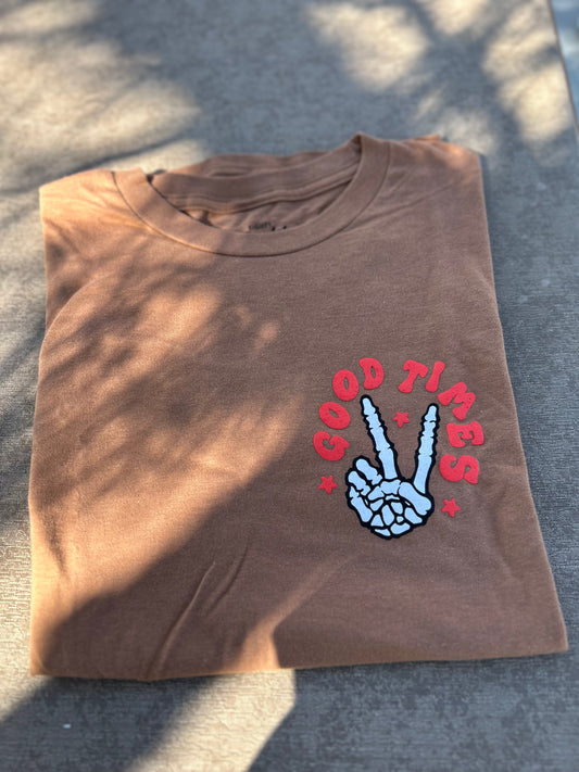 Folded brown t-shirt with 'Good Times' and peace sign design on a textured surface