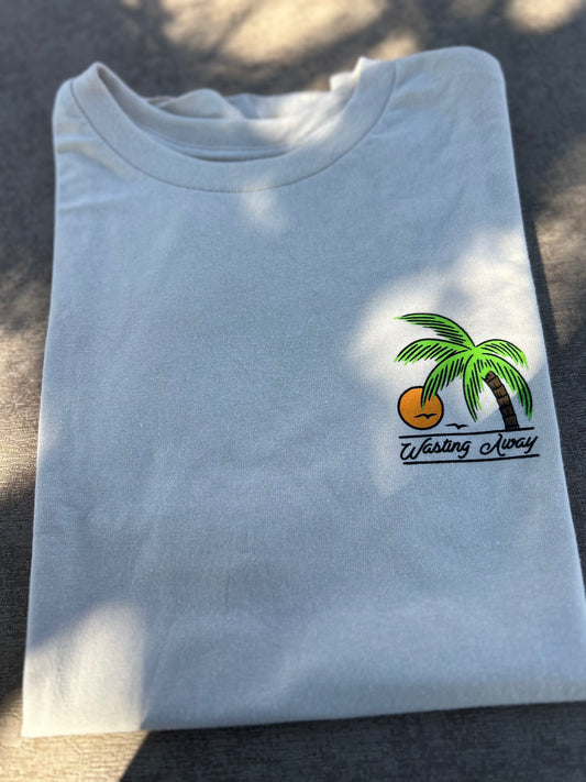 Folded cream colored t-shirt with a palm tree and sun design on a dark surface