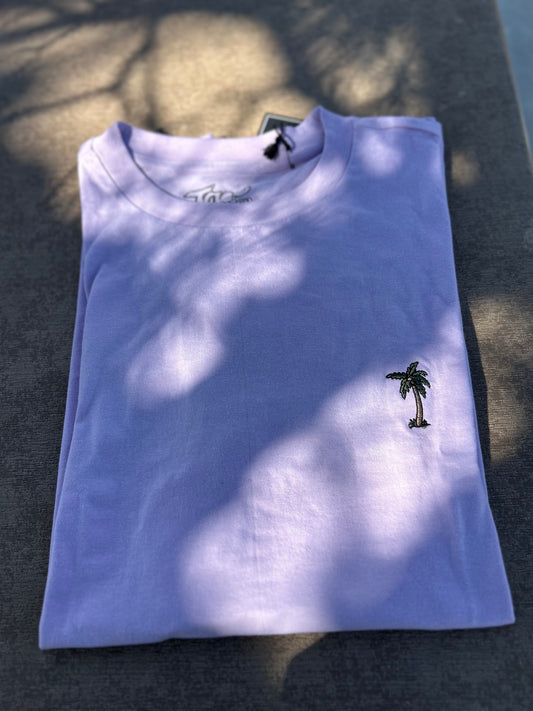 Folded light purple t-shirt with a palm tree design on a dark surface