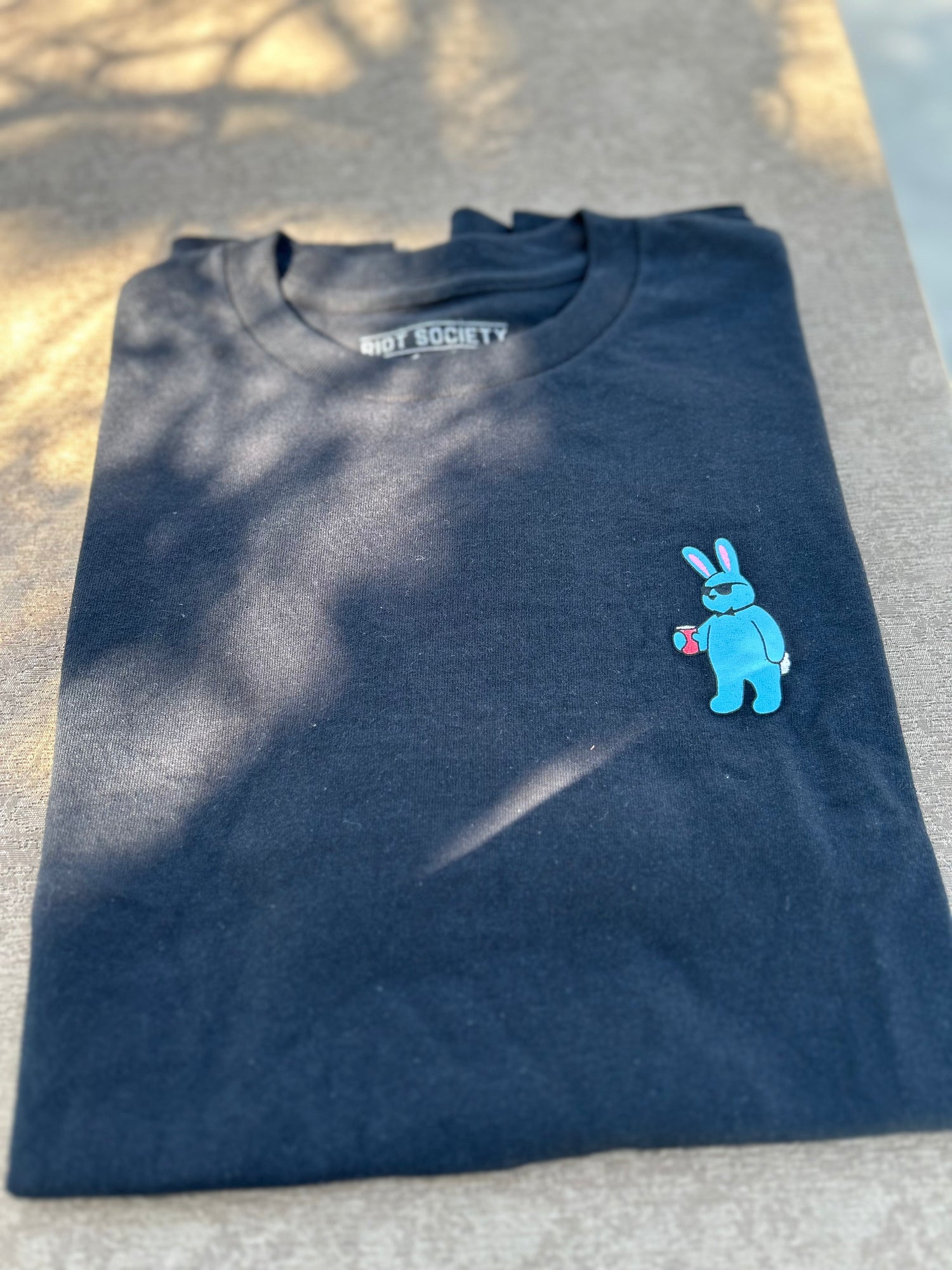 Folded black t-shirt with a blue cartoon character on a textured surface